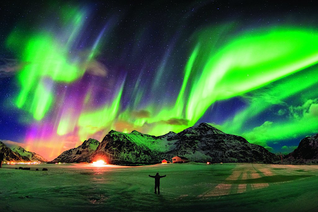 Aurora-borealis-Northern-lights-over-mountain-with-one-person-at-Skagsanden-beach-Lofoten-islands-Norway-By-Mumemories