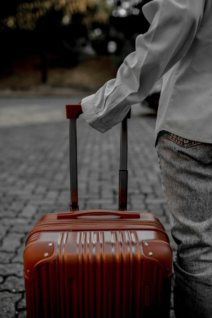 A person pulling a red suitcase on a cobblestone street, indicating travel or journey.