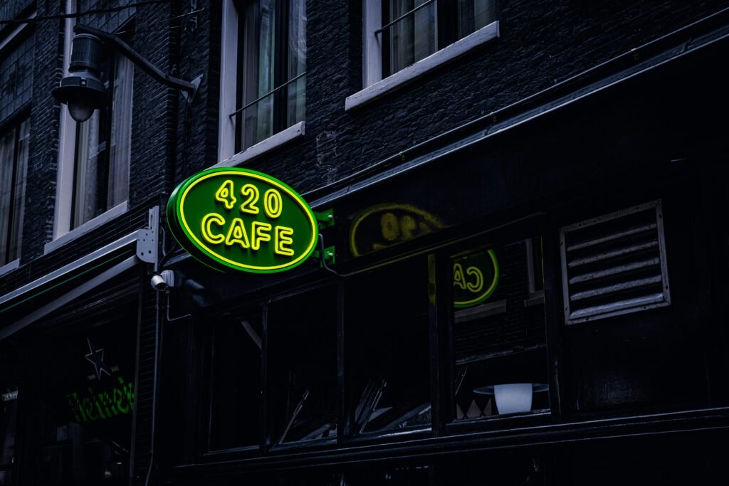 pexels-photo-3081946-3081946 Green neon sign '420 Cafe' on a building facade in Amsterdam, creating a vibrant city atmosphere.