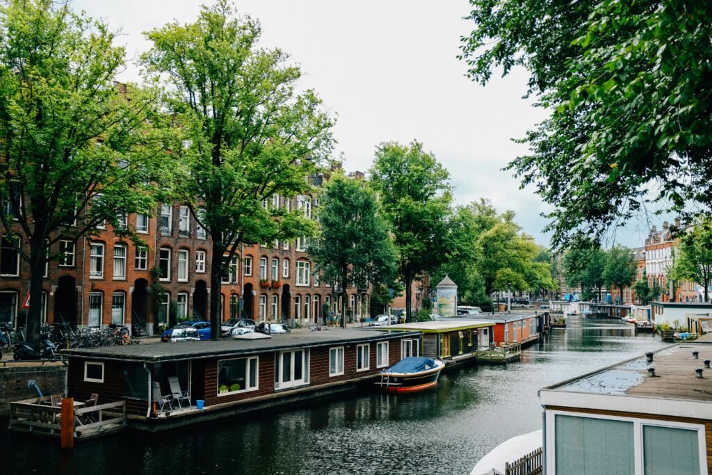 pexels-photo-3884479-3884479 Scenic canal in Amsterdam lined with houseboats and lush trees, capturing the city's unique charm.