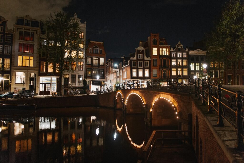 pexels-photo-5066418-5066418 Beautiful illuminated bridge and houses along Amsterdam's canal at night.