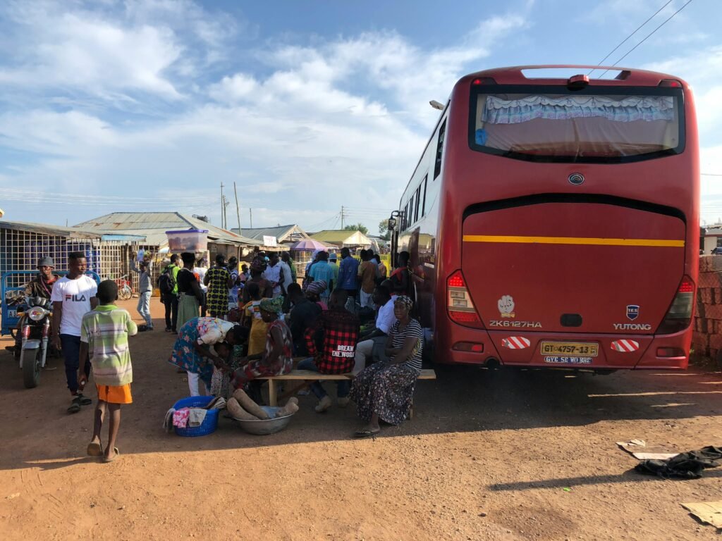 pexels-photo-8613993-8613993 A busy scene at a Ghanaian bus station with locals gathered around a parked bus on a sunny day.