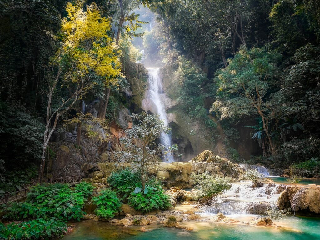 pexels-photo-1385474-1385474 Serene waterfall cascading through dense jungle in Laos, surrounded by vibrant foliage.