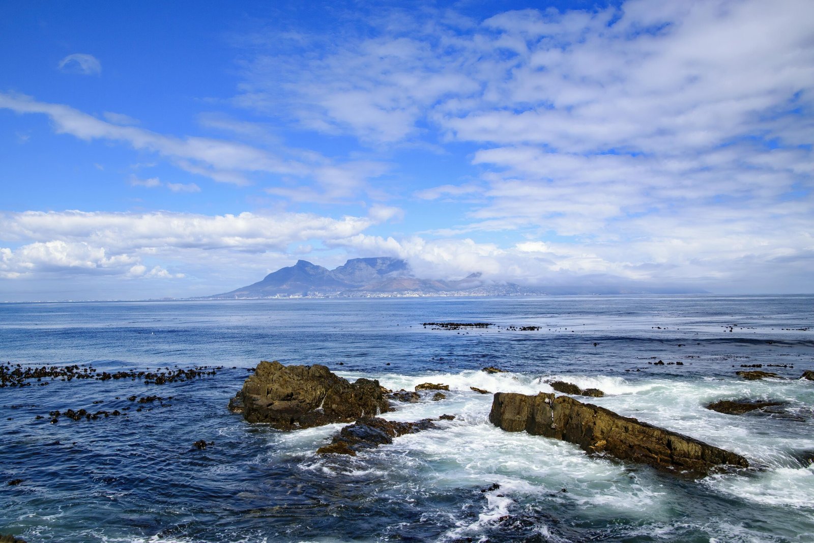 pexels-photo-14958837-14958837 Stunning view of waves and rocks on Robben Island, with Table Mountain visible across the sea.