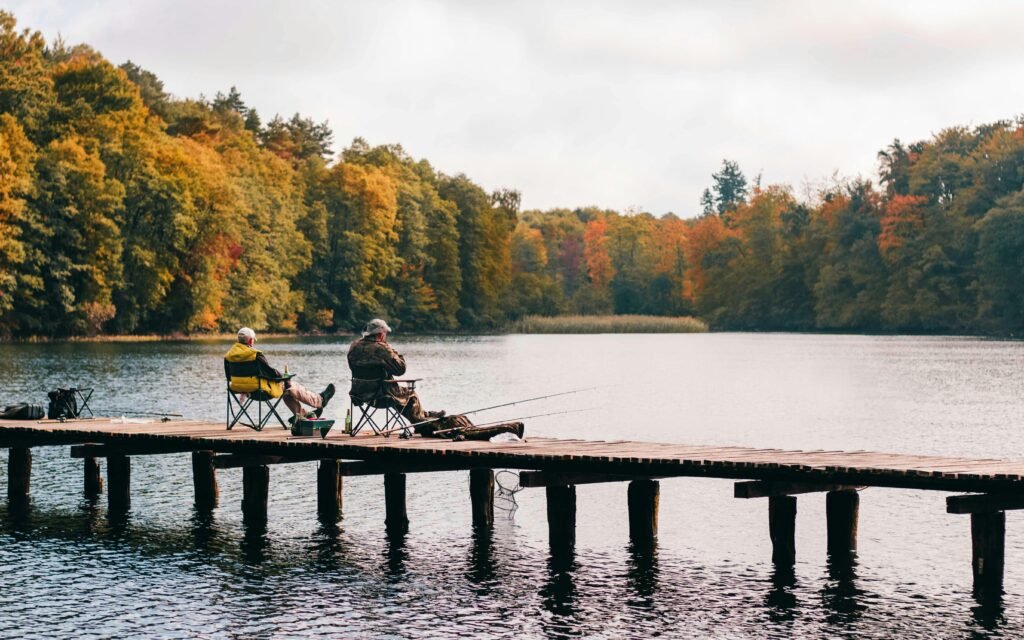 pexels-photo-1630039-1630039 Two men fishing on a pier surrounded by autumn foliage at a scenic lake.