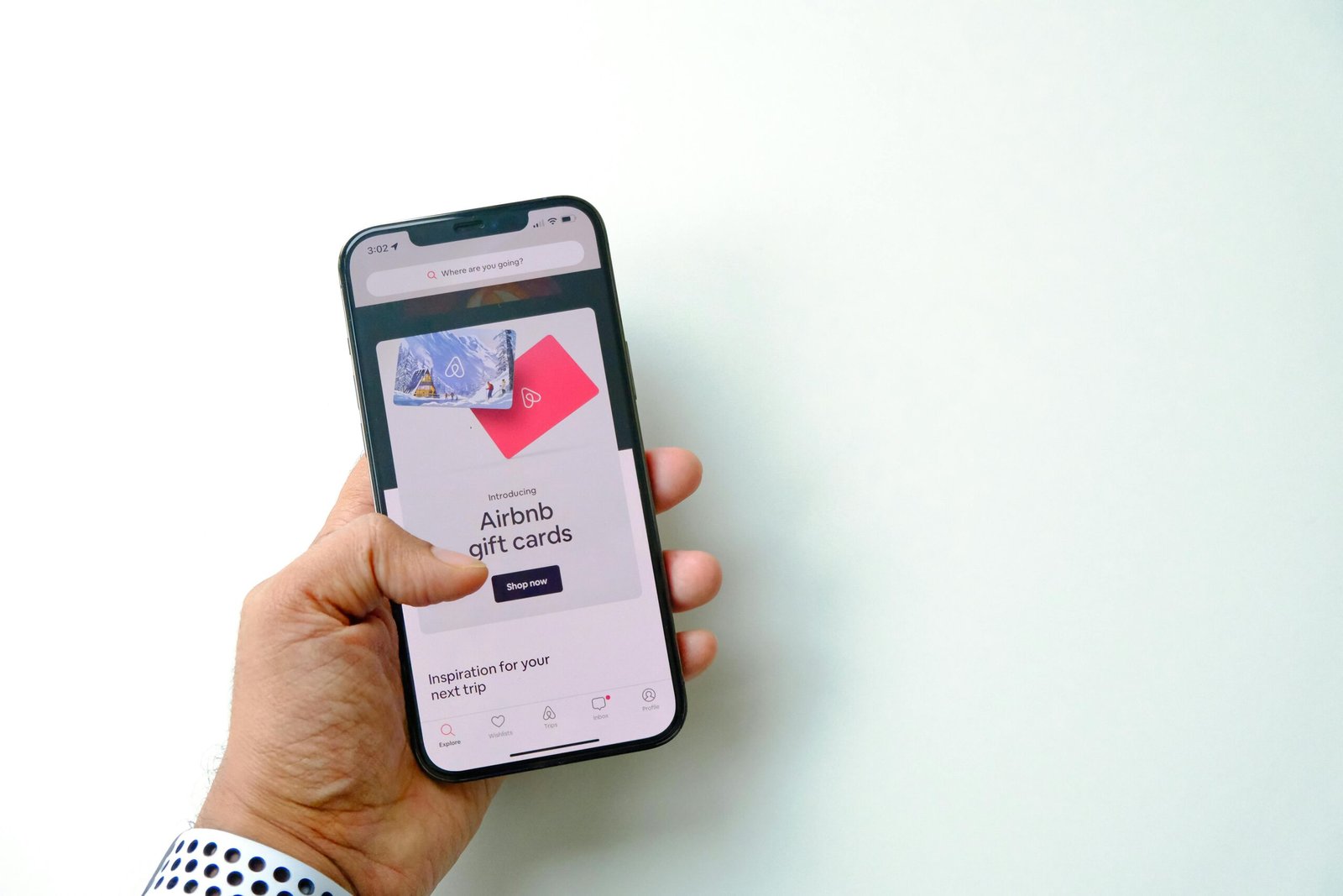 Close-up of a hand holding a smartphone displaying Airbnb gift cards on a white background.