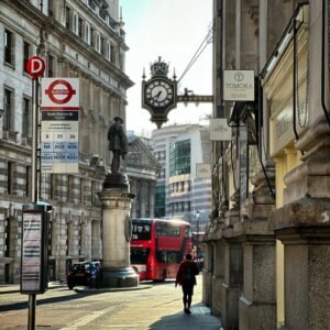 Busy London street scene with a red double-decker bus, clock, and statue.