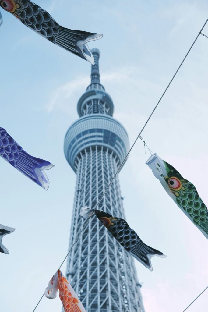 A low angle view of Tokyo Skytree framed by colorful carp streamers against a clear sky.