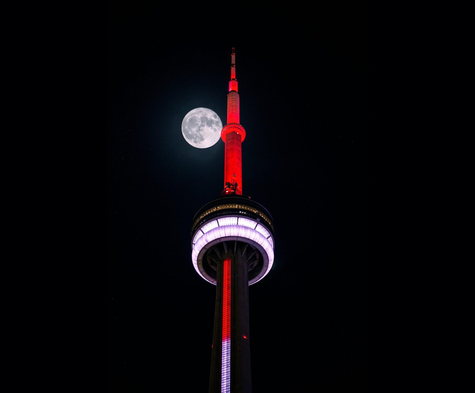 pexels-photo-234824-234824 Iconic CN Tower lit up in red with a full moon in Toronto's night sky.