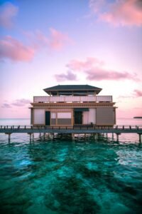 Stunning overwater villa at sunset in the Maldives with vibrant skies and turquoise waters.