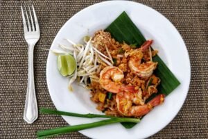 Delicious Pad Thai with shrimps, bean sprouts, and lime on a banana leaf, served on a woven mat.