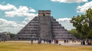 A view of El Castillo Pyramid at Chichen Itza with tourists exploring. Iconic Mayan archaeology.