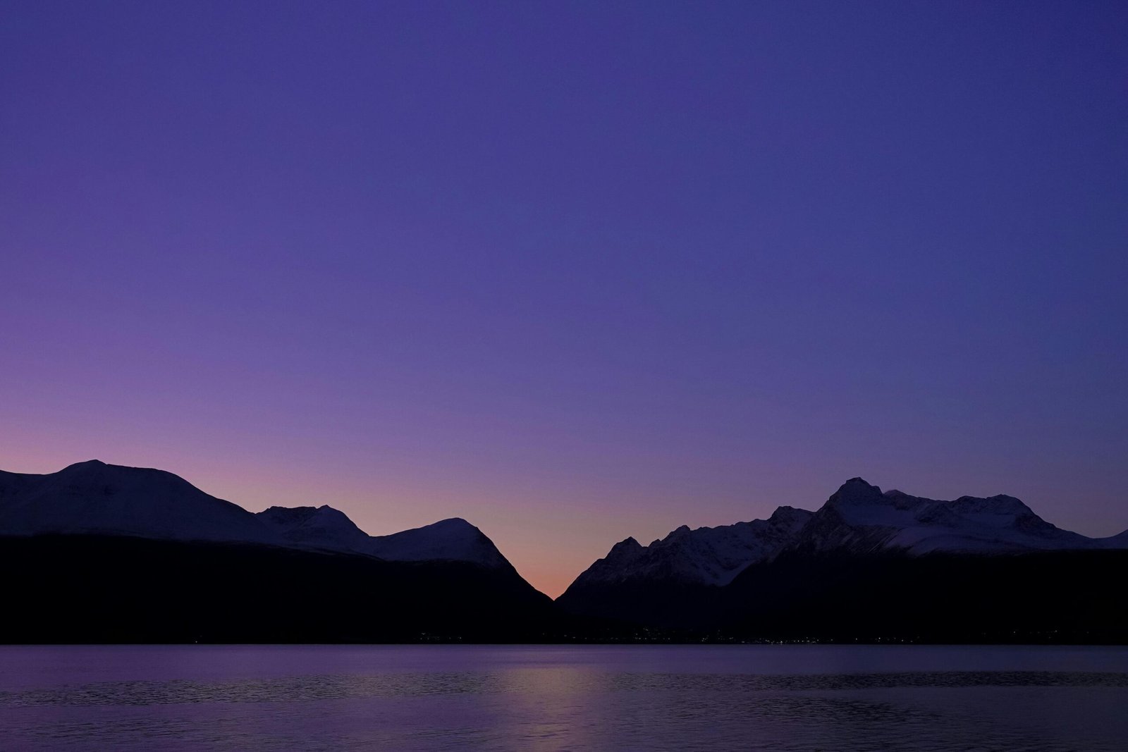 pexels-photo-31539189-31539189 A tranquil Norwegian twilight scene featuring mountain silhouettes against a purple sky.
