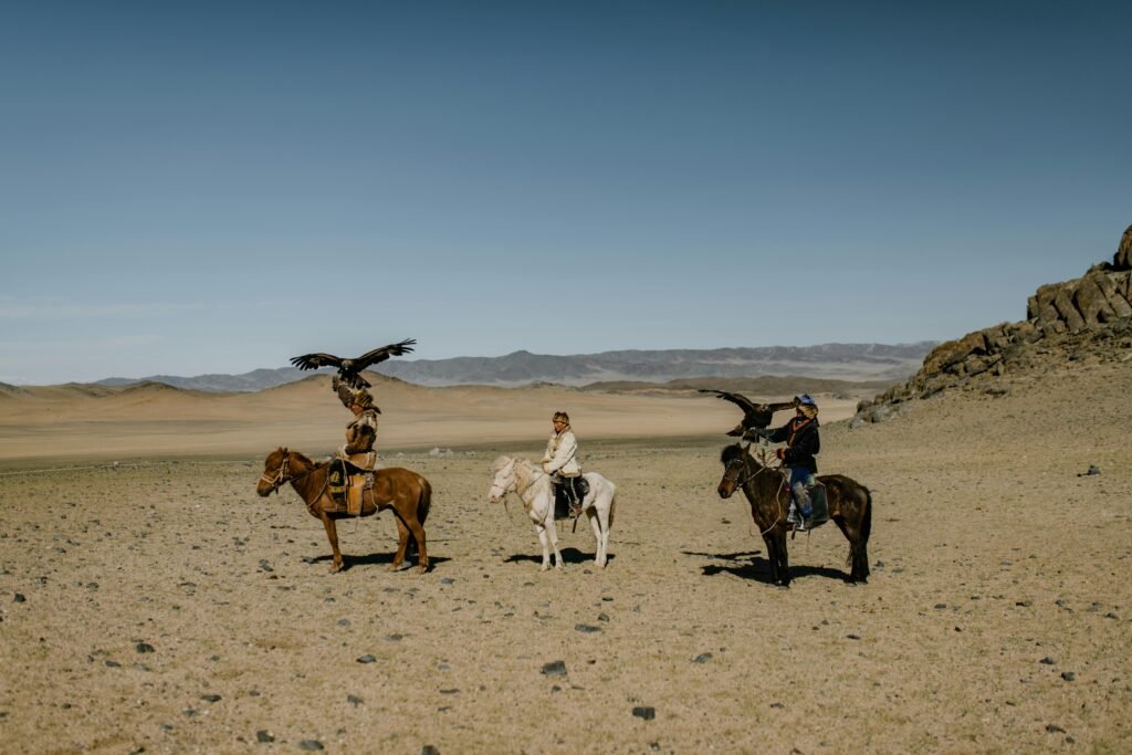 pexels-photo-5275365-5275365 Traditional Mongolian eagle hunters on horseback in the vast desert landscape.