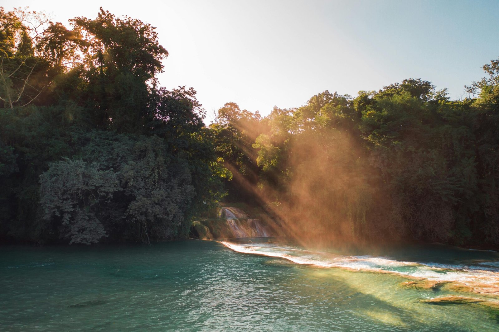 pexels-photo-6943664-6943664 A peaceful waterfall cascades amidst lush forest with beams of sunlight streaming through, creating a tranquil scene.