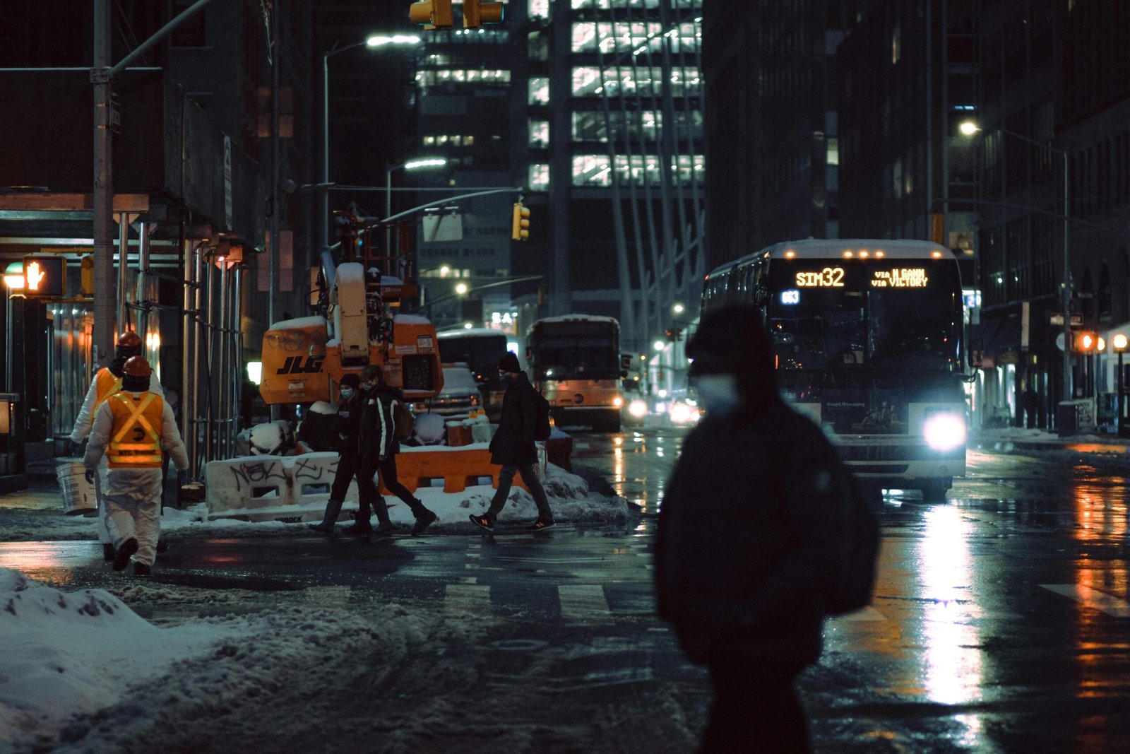 pexels-photo-7079360-7079360 People in medical masks strolling on crosswalk near roadway with glowing buses on dark street during winter evening in city