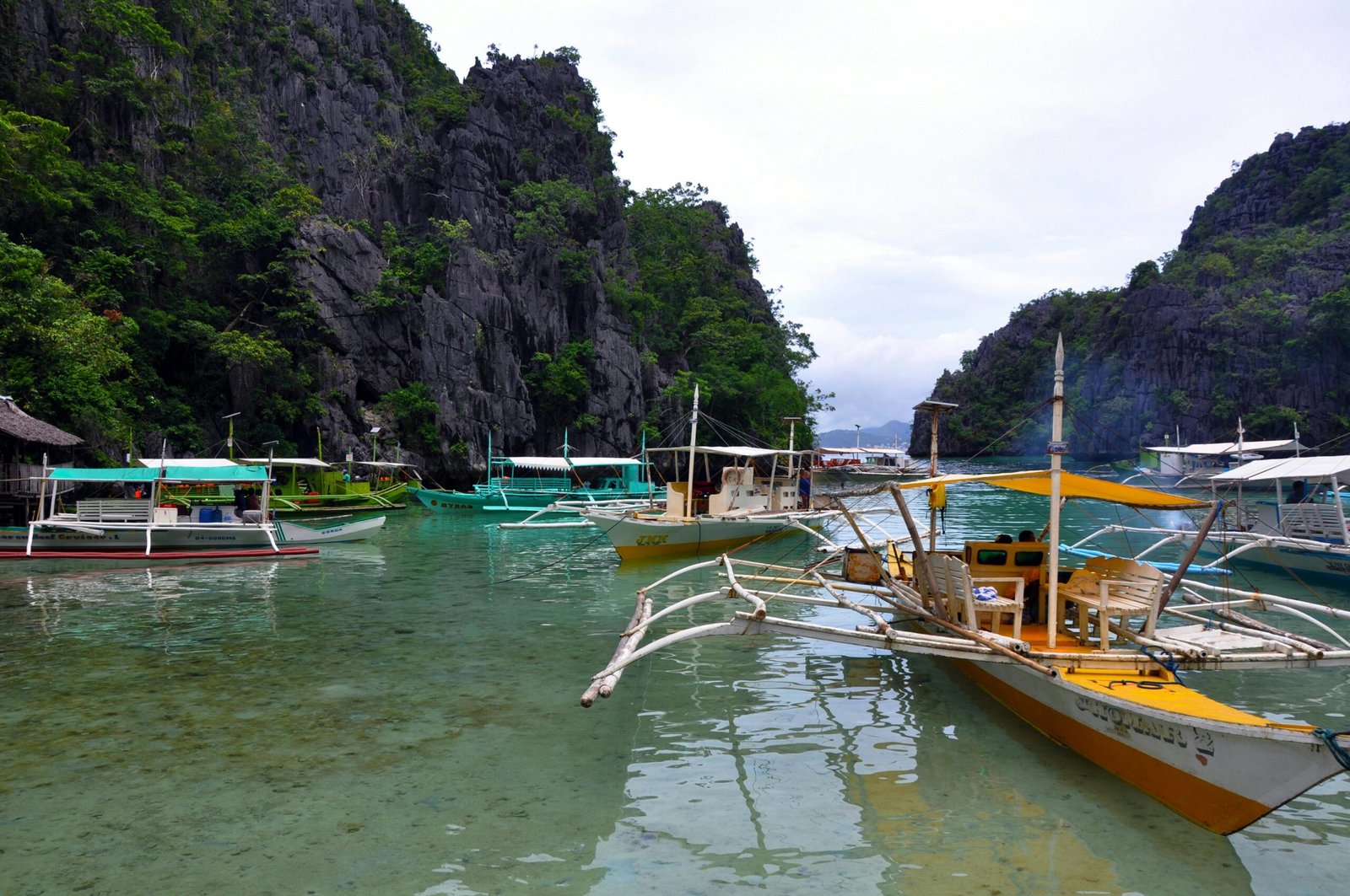 pexels-photo-12267682-12267682 Vibrant traditional boats floating on the clear waters of El Nido, Philippines, surrounded by lush cliffs.