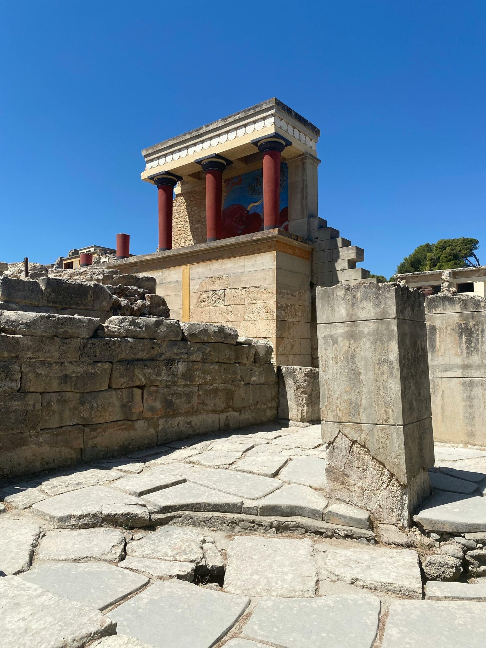 pexels-photo-14320445-14320445 Explore the ancient ruins of Knossos Palace with vibrant red columns under a clear blue sky in Crete, Greece.