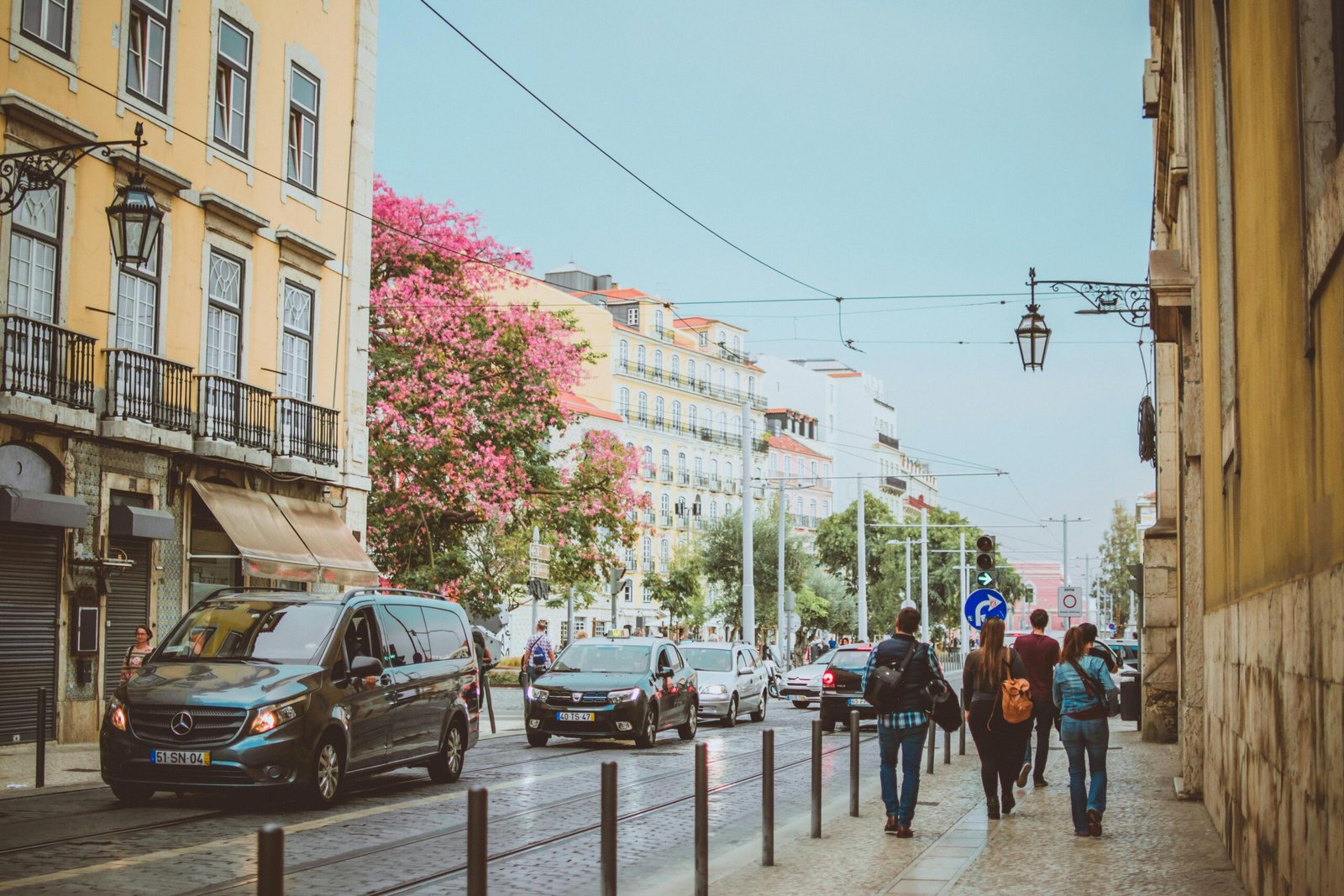 pexels-photo-1550347-1550347 Vibrant Lisbon street with pedestrians and vehicles under a clear sky.