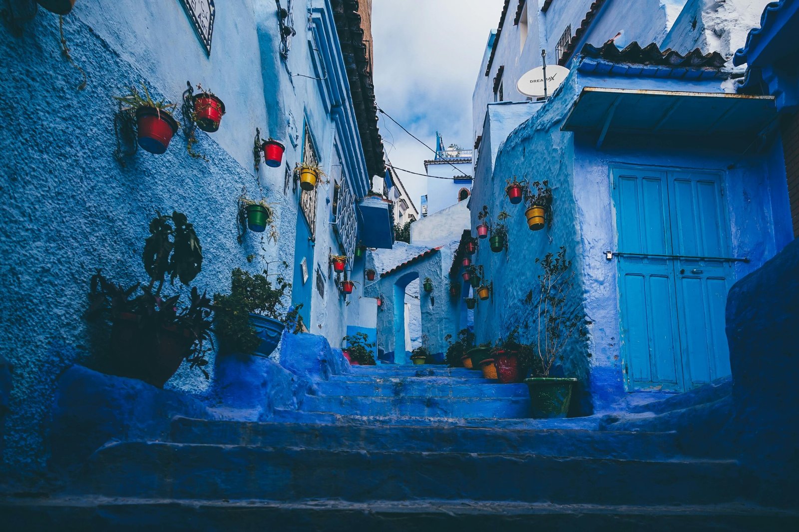 pexels-photo-1563277-1563277 Colorful pots line the blue-washed walls of a narrow alley in Chefchaouen, Morocco.