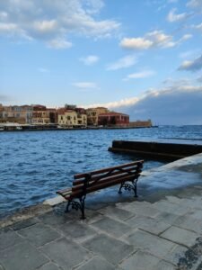 Peaceful scene of Chania harbor with a bench on the promenade overlooking the sea.
