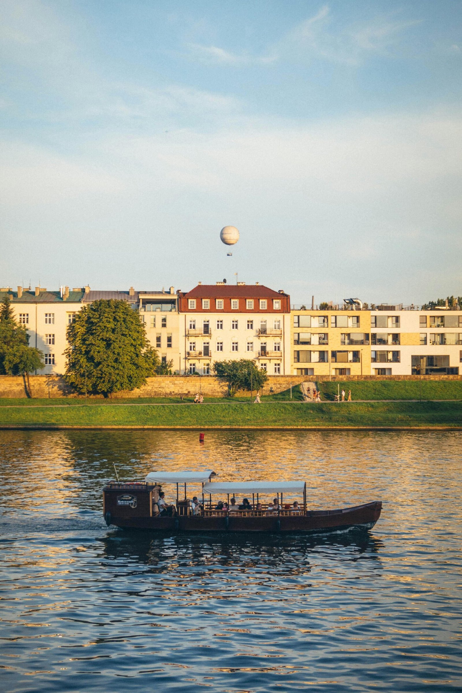 pexels-photo-18120825-18120825 Peaceful river tram sailing on Vistula River in Krakow with city skyline and balloon in the background.