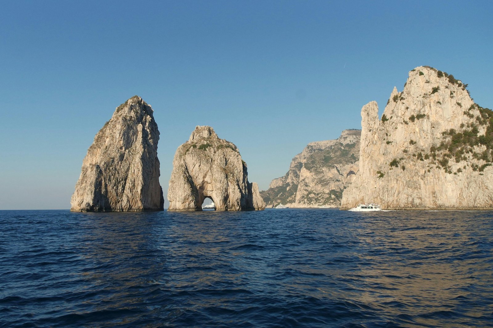 pexels-photo-20523049-20523049 Stunning view of the Faraglioni rock formations off the coast of Capri, Italy, under a clear blue sky.