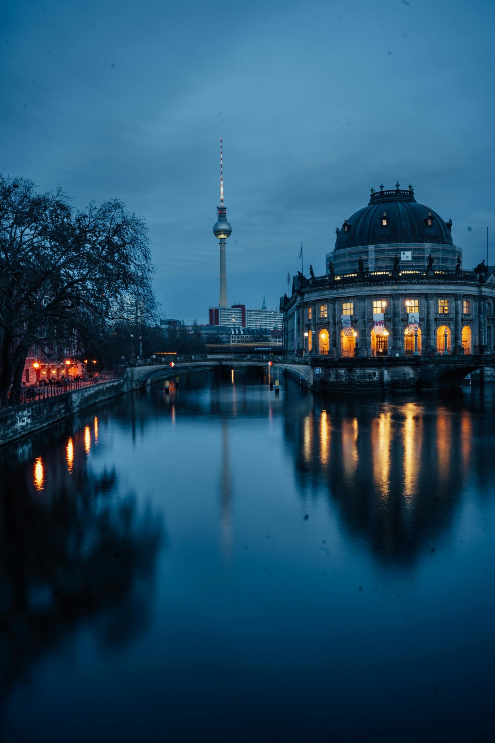 Dramatic evening view of Berlin's Fernsehturm and Bode Museum reflecting in the Spree River.