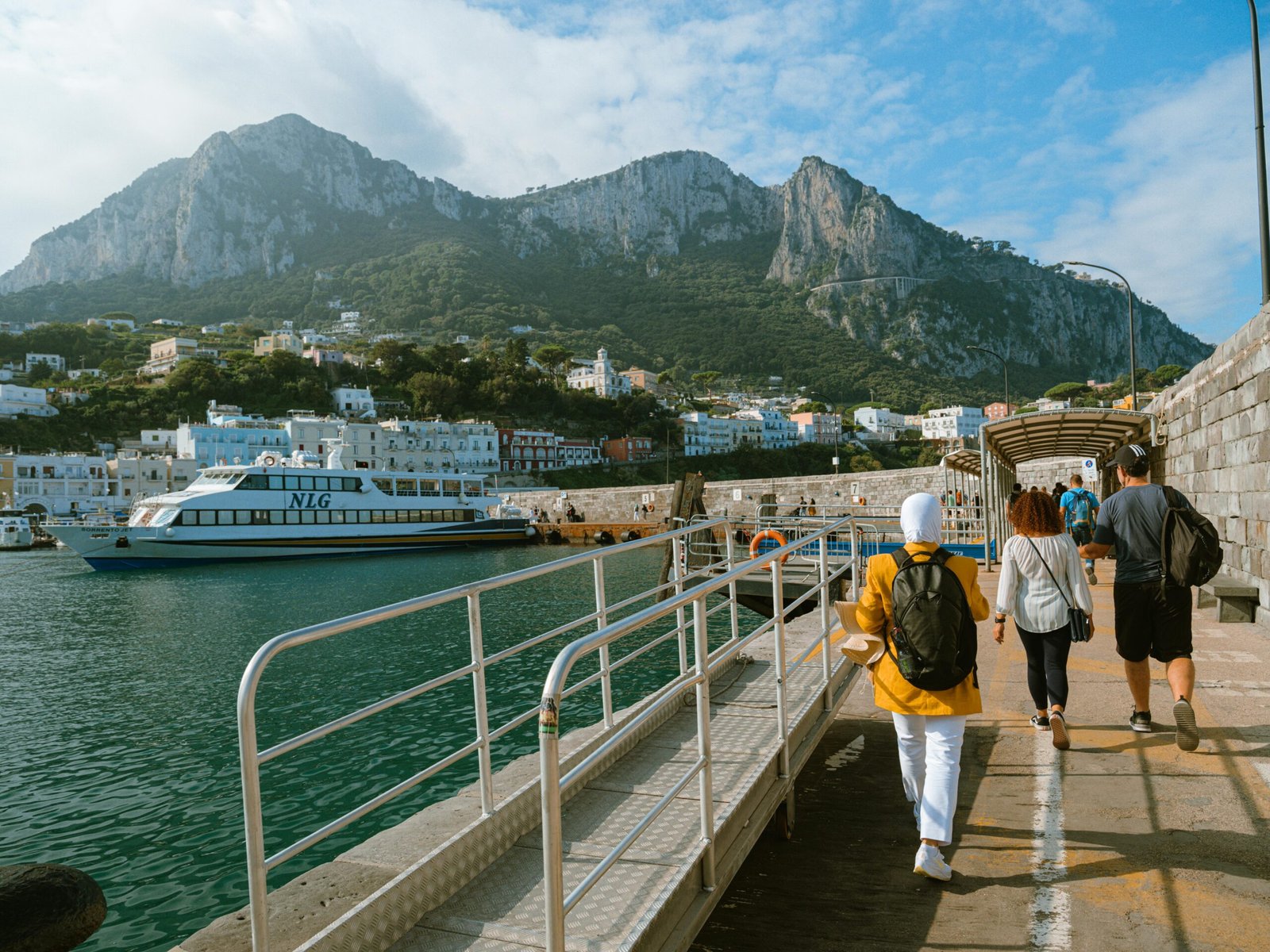 pexels-photo-27064846-27064846 A picturesque view of tourists walking on the pier of Capri Island, Italy, with mountains and sea.