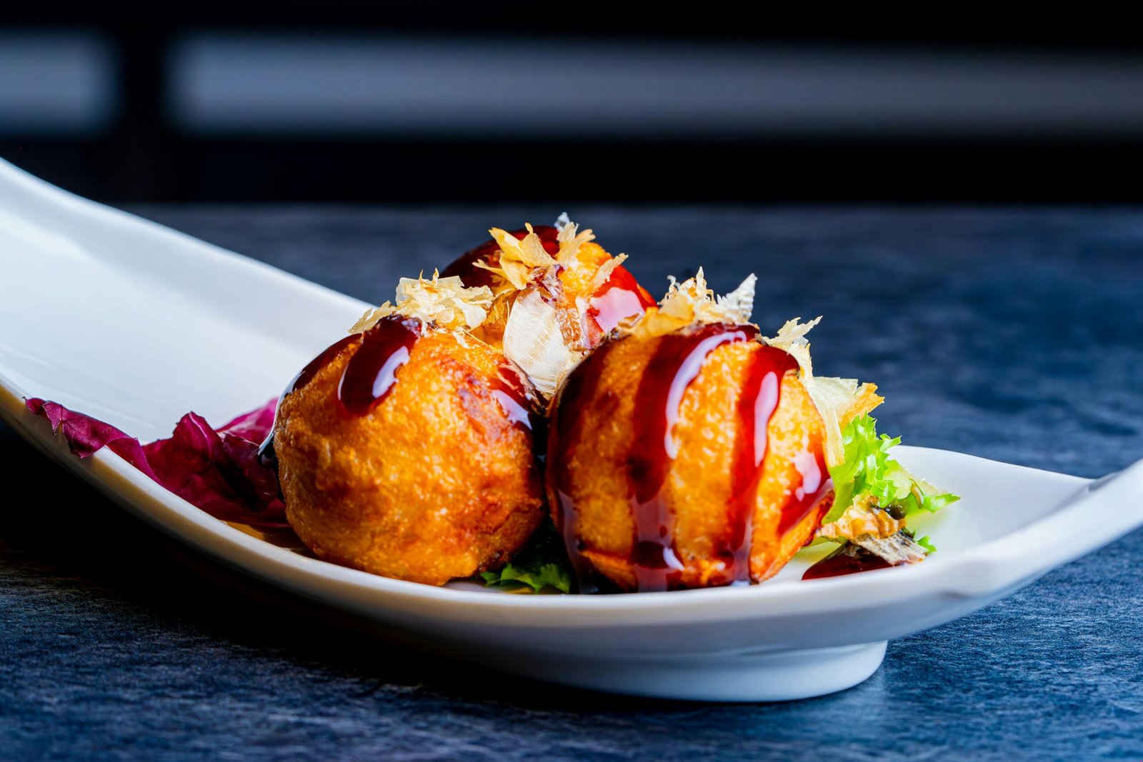 pexels-photo-28460875-28460875 Crispy takoyaki balls drizzled with sauce on a white plate, a Japanese street food delight.