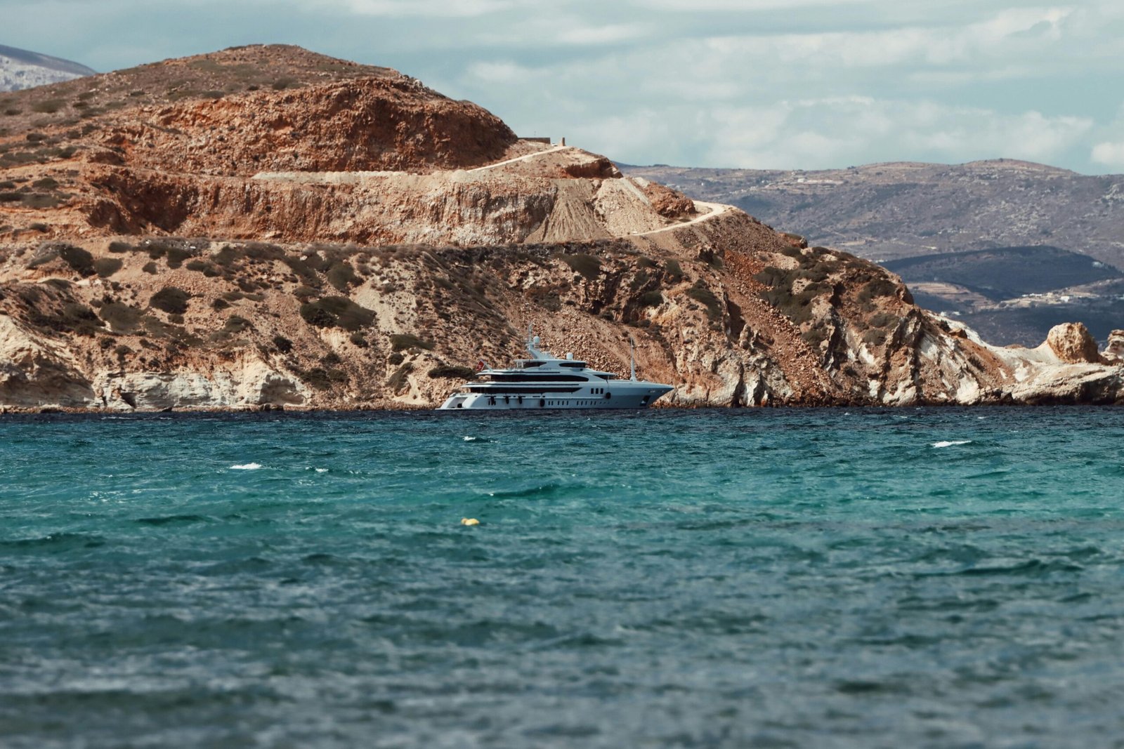 pexels-photo-30275261-30275261 A stunning luxury yacht cruising near the rocky shores of Naxos, Greece, under clear azure skies.