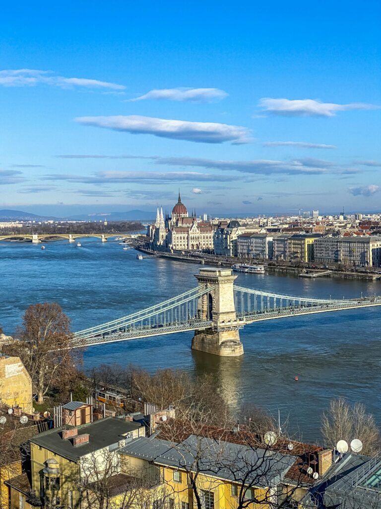 Aerial view of Budapest's iconic Szechenyi Chain Bridge spanning the Danube River under a bright blue sky.