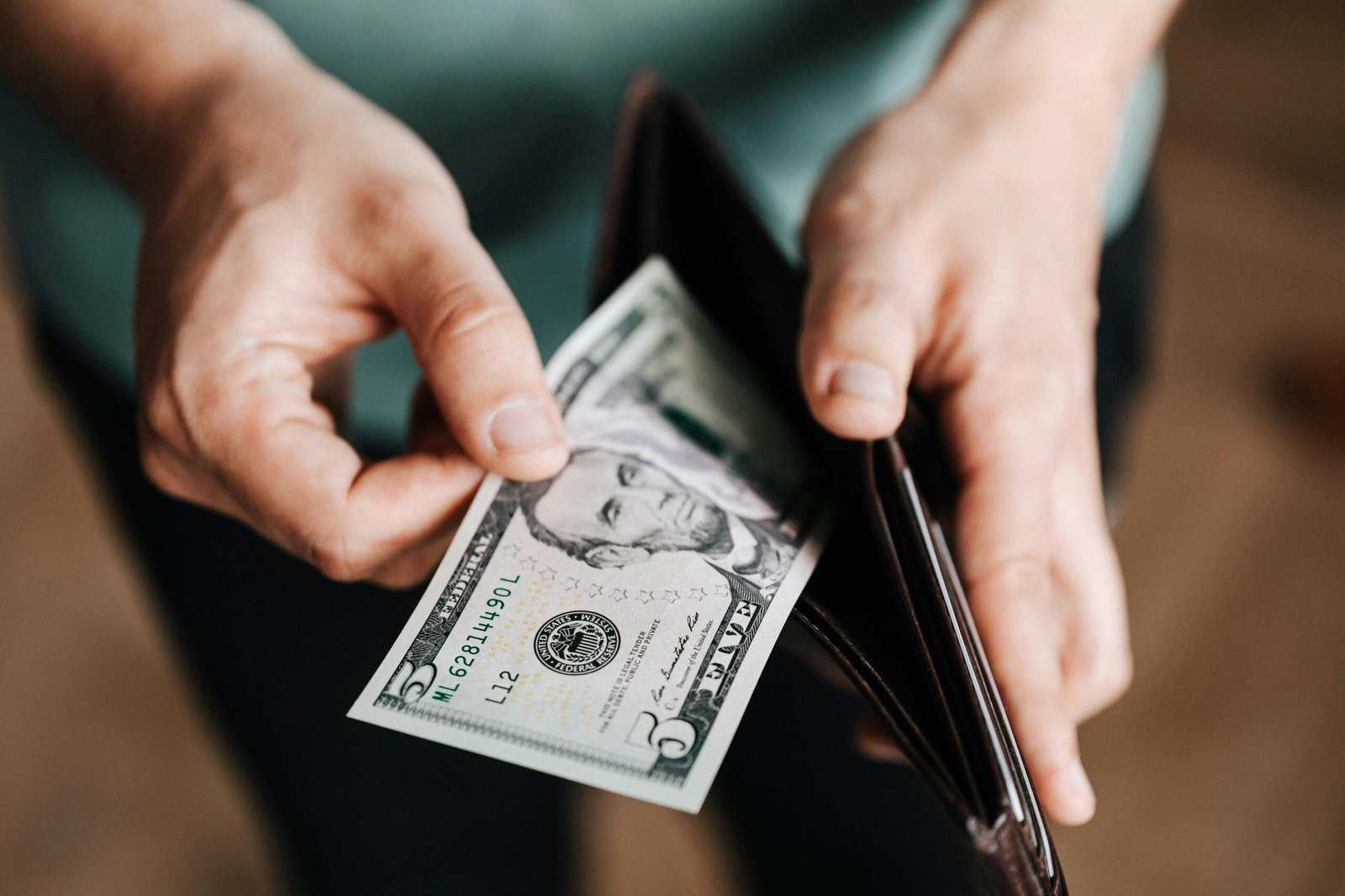 pexels-photo-4386421-4386421 A person taking a five dollar bill from a wallet symbolizing personal finance and budget management.