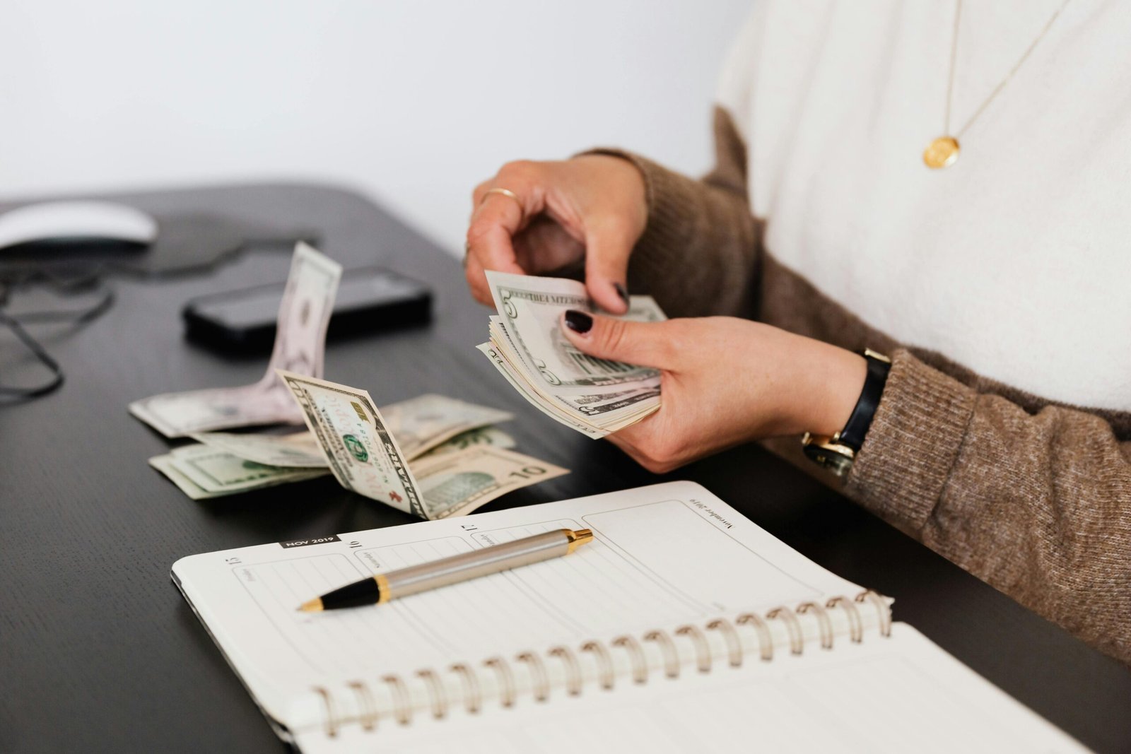 pexels-photo-4475523-4475523 Close-up of person counting cash with notepad on desk, indicating financial tasks.