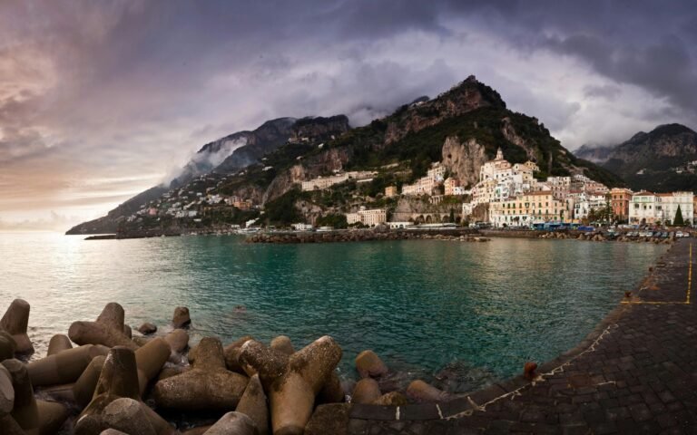 Stunning view of Amalfi coastal town against a dramatic sunset sky, perfect for travel and nature themes.