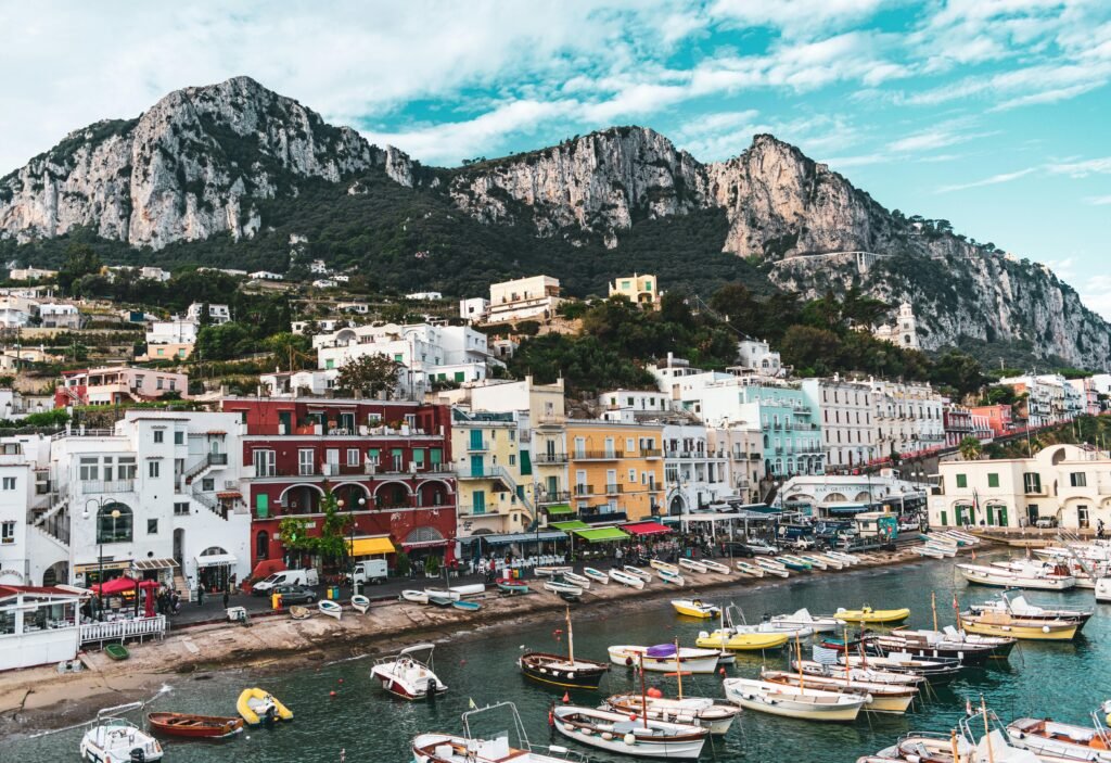 Scenic view of colorful buildings and boats along Capri's marina with towering cliffs in the background.