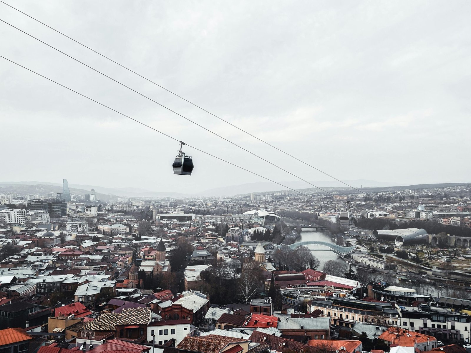 pexels-photo-12925880-12925880 Aerial view of Tbilisi's skyline with a cable car above the urban landscape, showcasing Georgia's architectural blend.