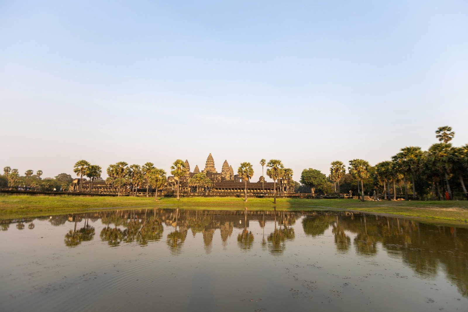 pexels-photo-15890572-15890572 Stunning sunrise over Angkor Wat temple with reflective water and palm trees.