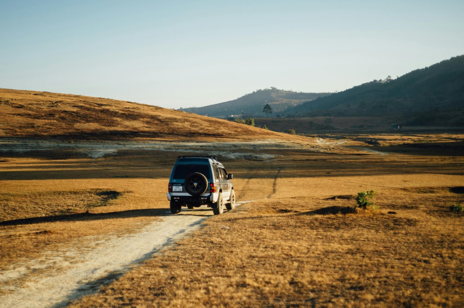 pexels-photo-18207343-18207343 SUV traveling on a dusty path in a remote, barren landscape under clear sky.