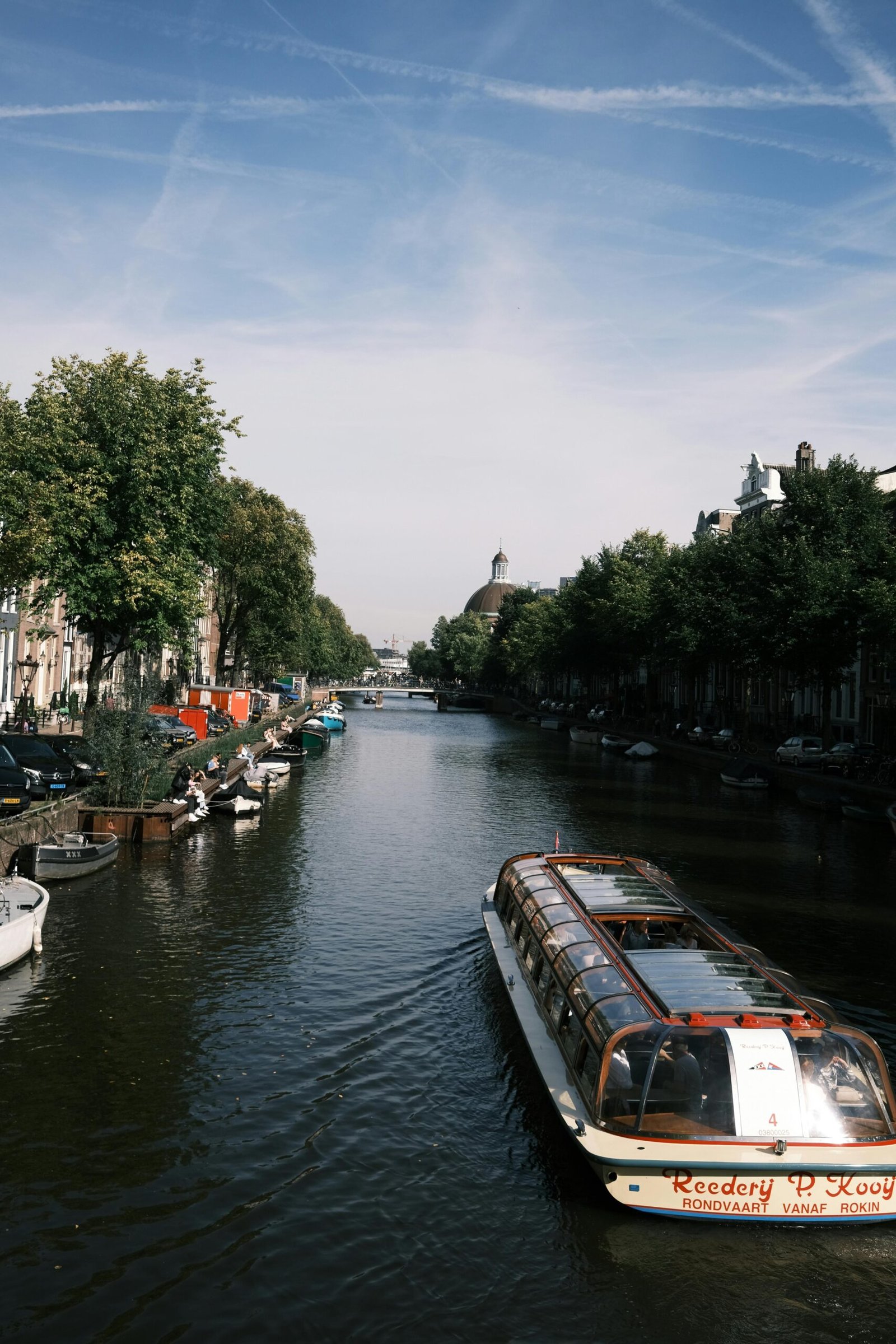 pexels-photo-18678536-18678536 Tourist barge navigating a canal in Amsterdam with scenic views of the city, trees, and boats.