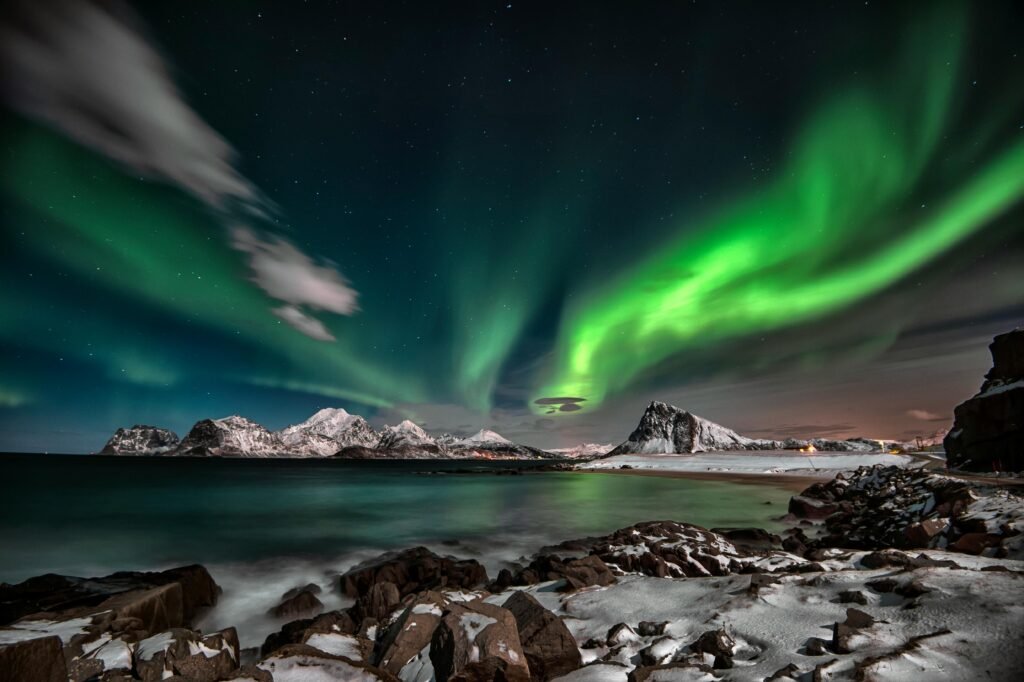 Mesmerizing aurora borealis illuminating a winter landscape with snowy mountains and a starry sky.