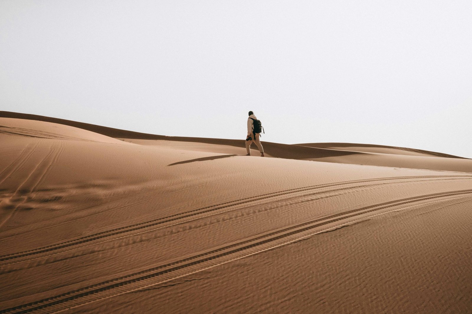 pexels-photo-20117735-20117735 A lone man hiking across vast desert sand dunes with a backpack, showcasing adventure.