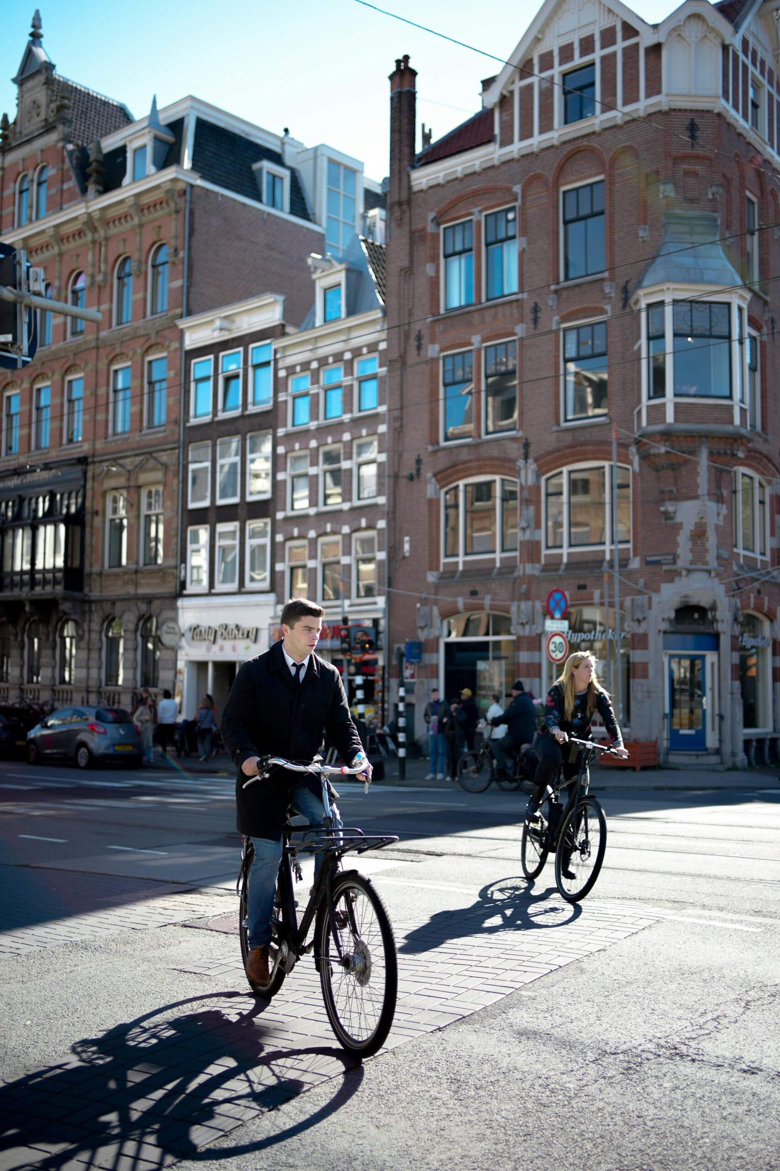 pexels-photo-28900290-28900290 Cyclists enjoy a sunny day in Amsterdam, showcasing the city's iconic architecture.
