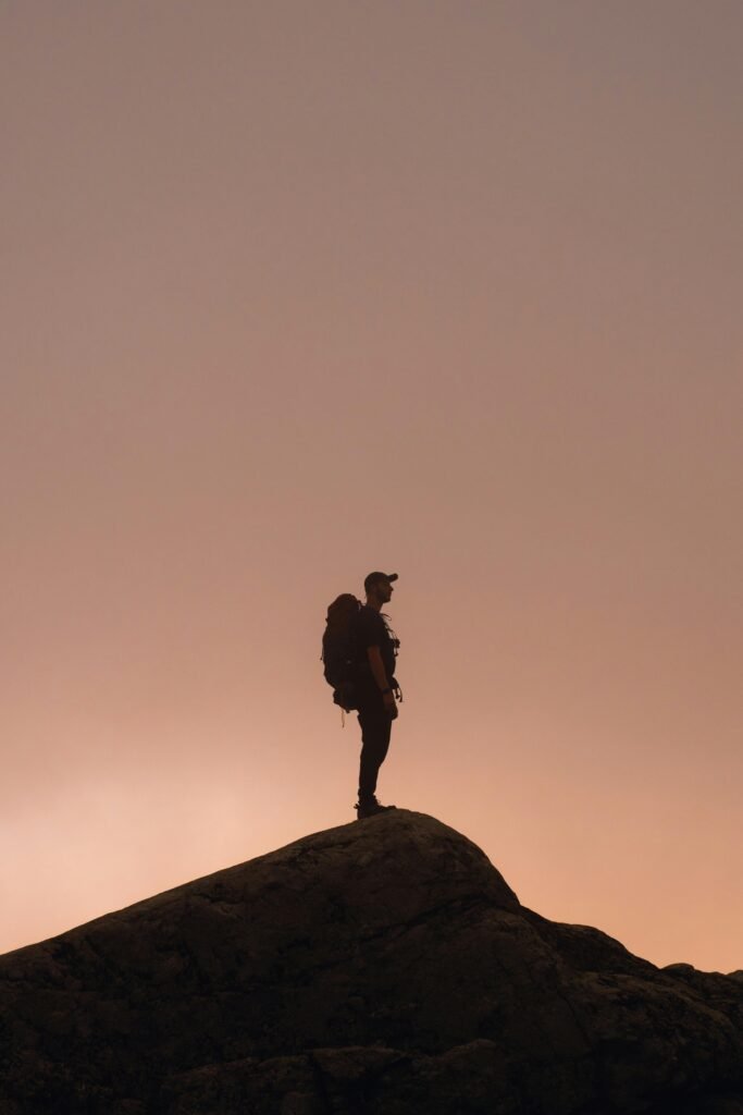 A lone hiker silhouetted against a dramatic sunset sky on a mountain peak, symbolizing adventure.