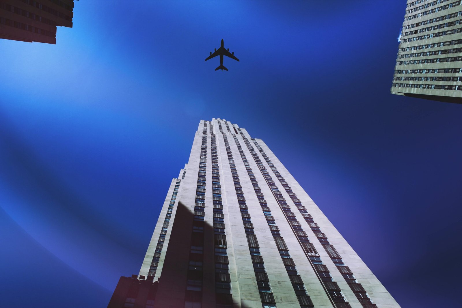 pexels-photo-437350-437350 A striking upward view of a New York skyscraper with an airplane flying above against a clear blue sky.