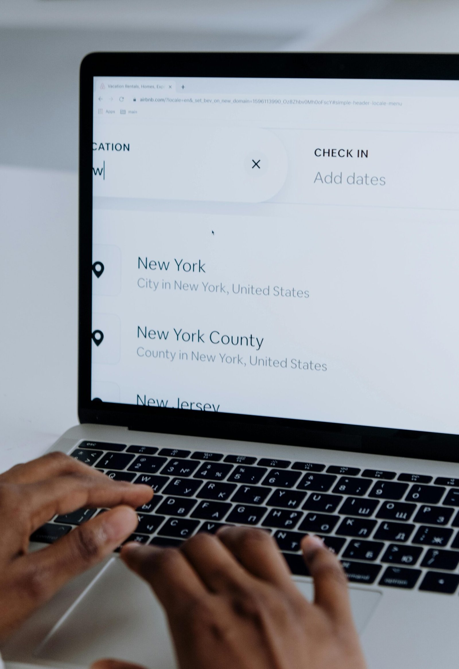 pexels-photo-5077040-5077040 Hands typing on a laptop near New York location search screen.