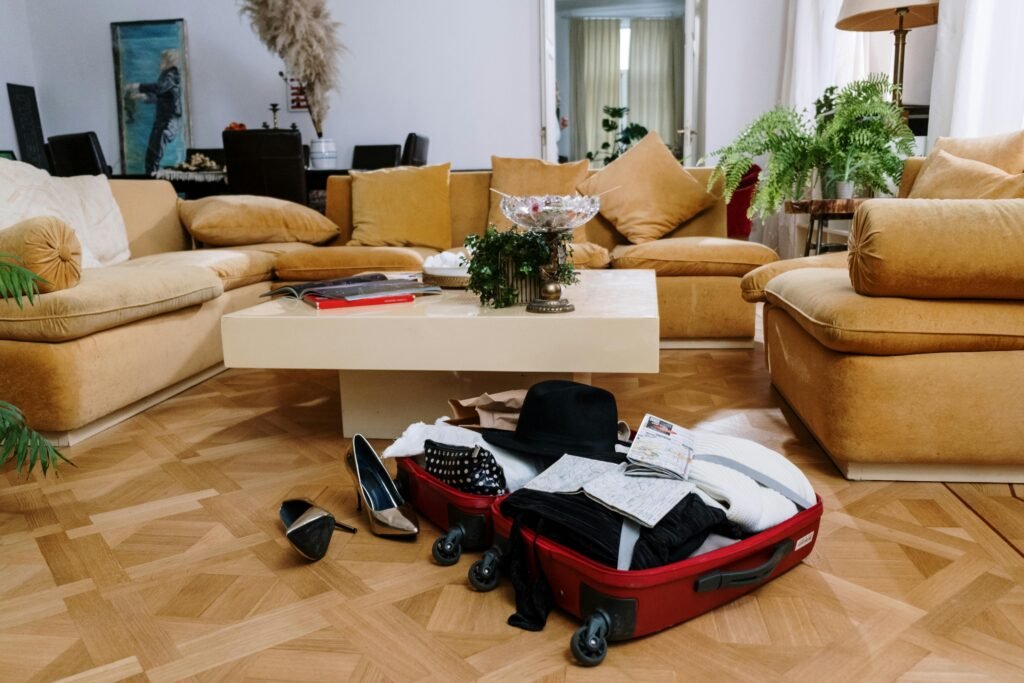pexels-photo-6551706-6551706 A stylish living room with beige couches and an open suitcase on a parquet floor, surrounded by plants.