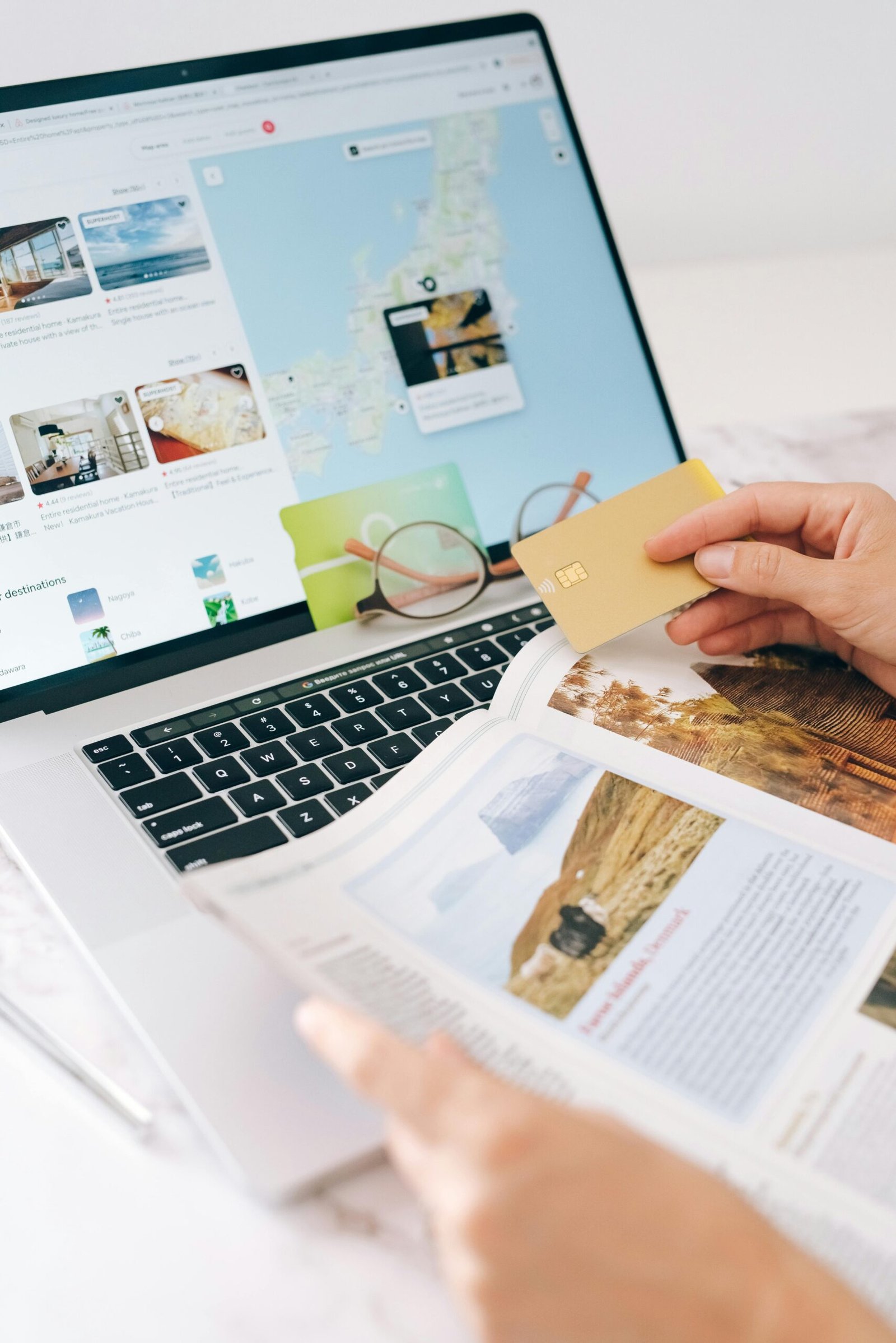pexels-photo-8937451-8937451-1 Hands holding credit card over laptop and magazine for online shopping and travel planning.