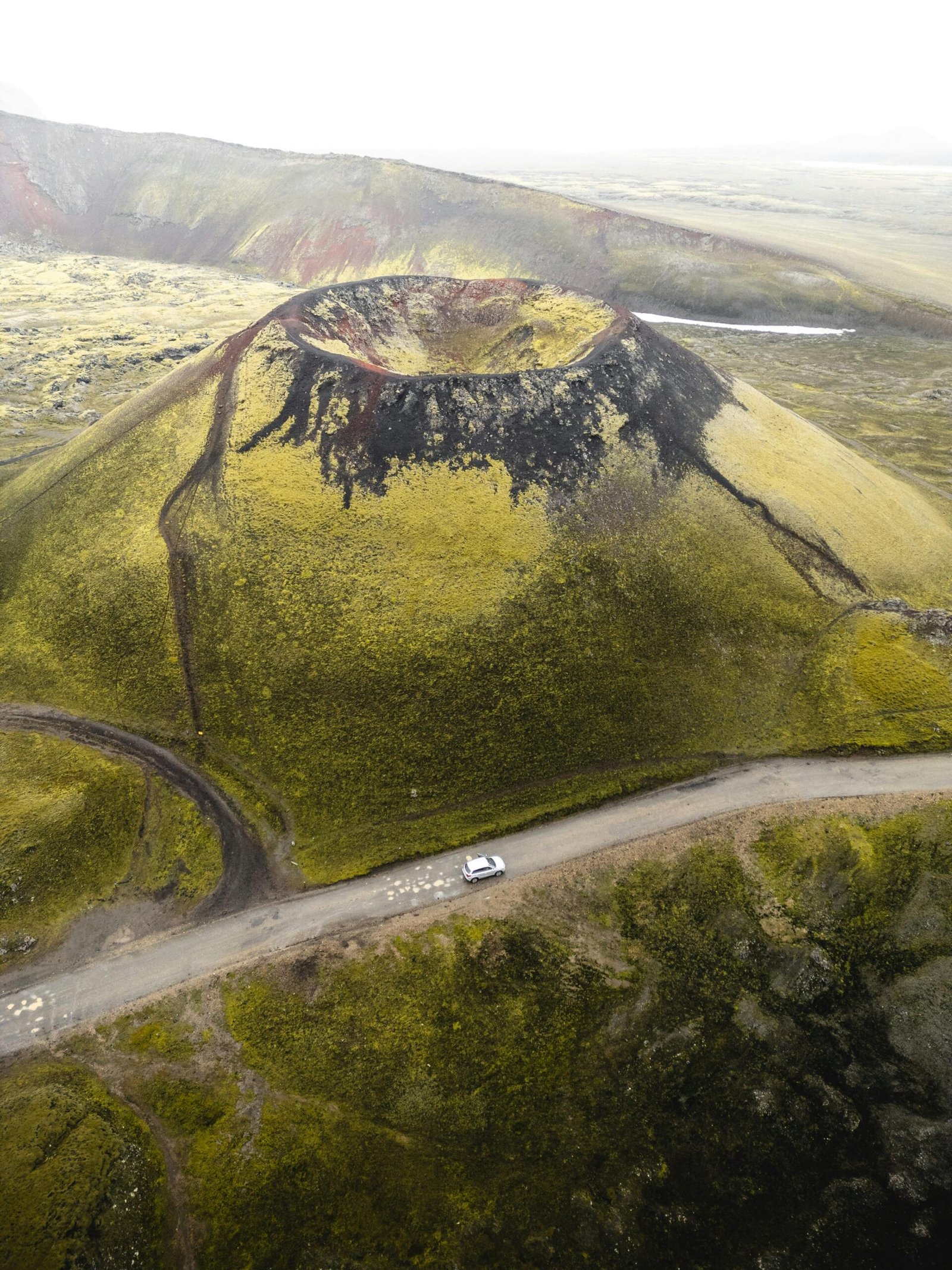 Aerial view of Grábrók volcano with a car on a dirt road, in rural Icelandic scenery.