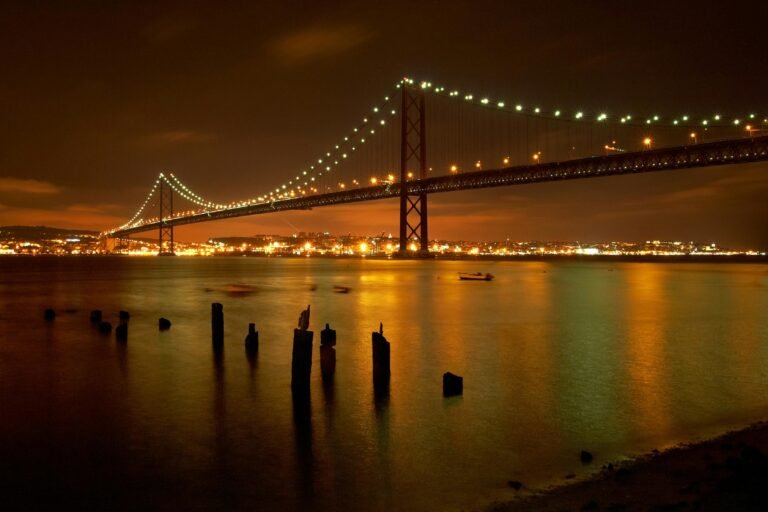 View of the illuminated suspension bridge spanning over the river in Lisbon during the night.